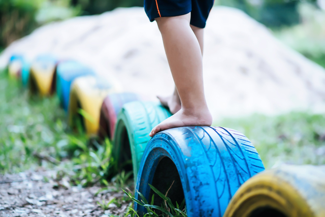 Child balancing on tyres during outdoor play, supporting gymnastics for school readiness, gross motor development, and physical readiness for school.