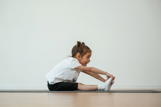 Preschool child stretching during a gymnastics activity, supporting gymnastics for school readiness, gross motor development, and physical readiness for school.