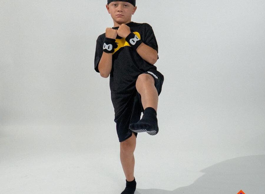 A child balancing on one leg with the other knee lifted, wearing Ninja Parkour kit.