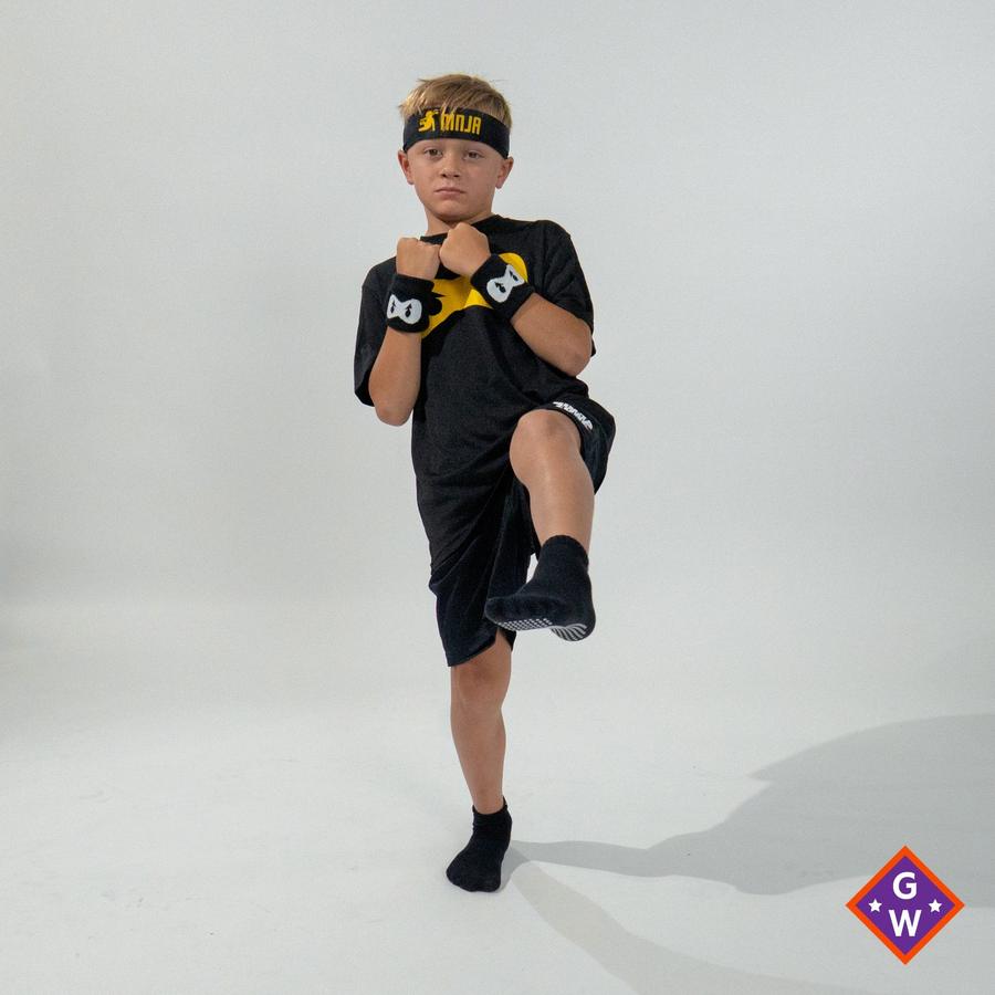 A child balancing on one leg with the other knee lifted, wearing Ninja Parkour kit.