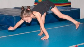 A child practising an animal walk on hands and feet on a blue mat, with the Gym Wizards logo.