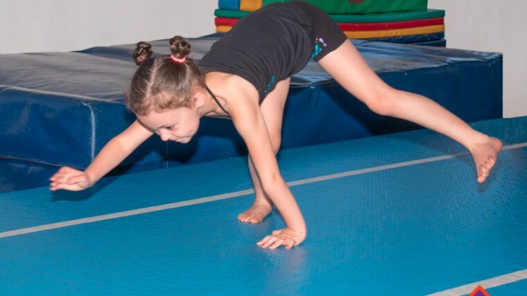 A child practising an animal walk on hands and feet on a blue mat, with the Gym Wizards logo.
